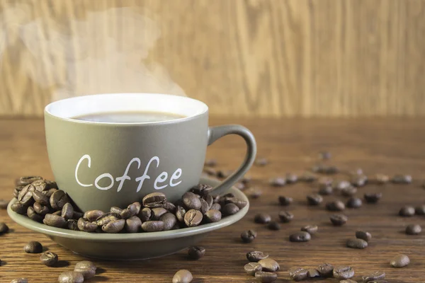 Eine Tasse Kaffee mit Bohnen steht auf einem Holztisch. verschwommen, — Stockfoto