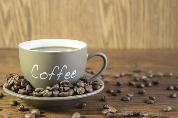 Eine Tasse Kaffee mit Bohnen steht auf einem Holztisch. verschwommen, — Stockfoto