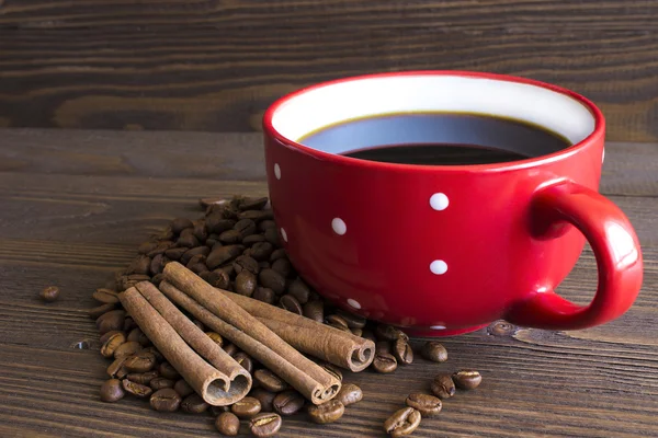 Kırmızı puantiyeli fincan kahve kahve çekirdekleri ve çubuk tarçın kabuğu yanında duruyor — Stok fotoğraf