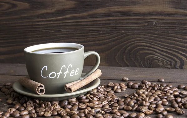 Eine Tasse Kaffee, Kaffeebohnen und Zimtstangen bellen auf einem alten Holztisch — Stockfoto
