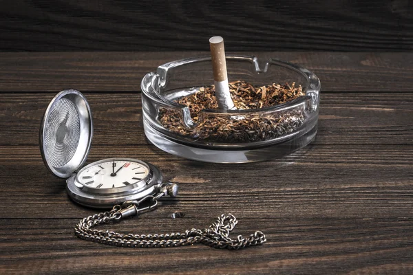 Vintage pocket watch en verfrommeld sigaret in glas asbak op de oude houten tafel — Stockfoto