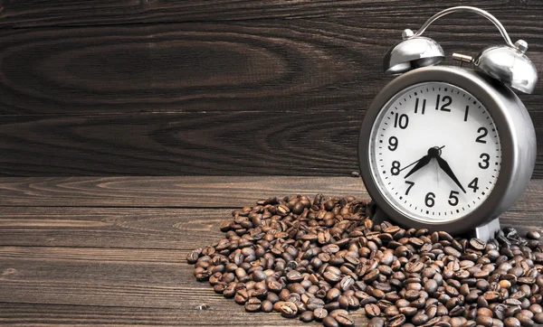 Reloj despertador con campanas y granos de café derramados sobre una vieja mesa de madera. Enfoque en dial —  Fotos de Stock