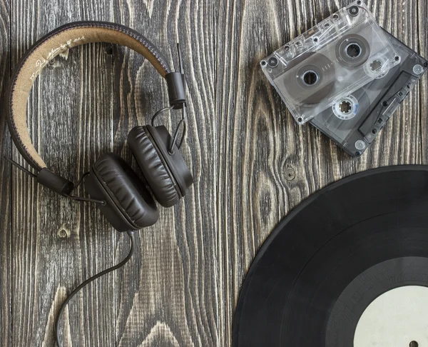 The musical equipment headphones audio cassette and  plate lie on a wooden table. Background Top view