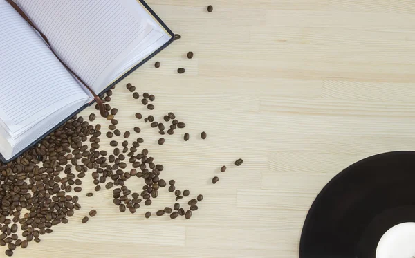 빈 메모장 검은 비닐 판 고 나무 바탕에 엎지른된 커피 콩. 상위 뷰 — 스톡 사진