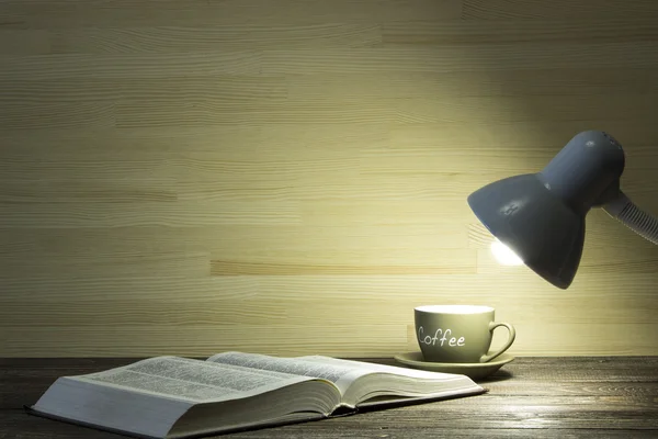 책과 커피 한잔 어두운 방에 있는 테이블에 램프에서 빛에 의해 조명 된다 — 스톡 사진