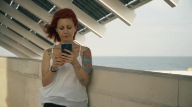 Kırmızı kafa ve sokakta onun akıllı telefon kullanan dövmeli kadın