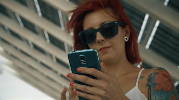 Mujer tatuada usando su teléfono inteligente con un gran panel solar UHD tiro — Vídeos de Stock