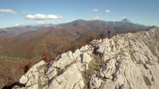 Un disparo aéreo de una mujer en la cima de una montaña de roca volando de cerca a lejos — Vídeo de stock