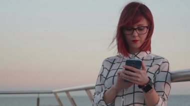 Kadın gözlük günbatımı sırasında bir akıllı telefon kullanan bir kıyı ortamı ile