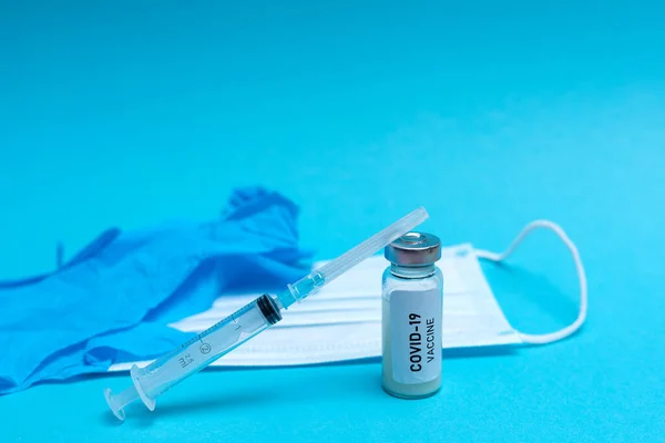 Dłoń w rękawiczce zawiera szczepionkę covid-19 na niebieskim tle — Zdjęcie stockowe