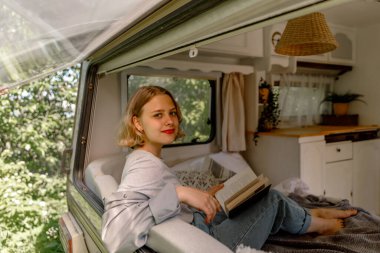 Genç bayan bir karavanda kitap okuyor, doğada, glamping, iyileşme