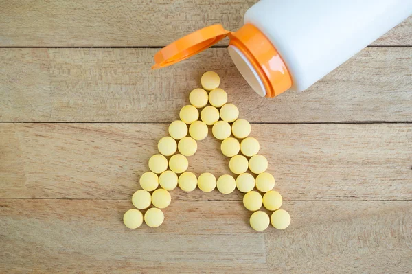 Geel pillen zelftappende vorm naar een alfabet op houten achtergrond — Stockfoto