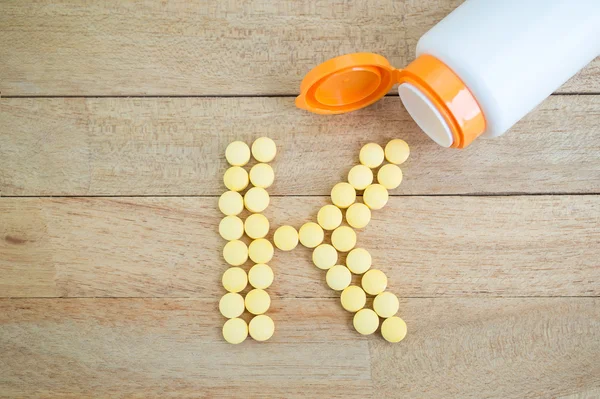 Yellow pills forming shape to K alphabet on wood background — Stock Photo, Image