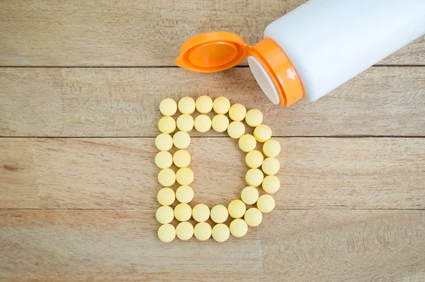 Yellow pills forming shape to D alphabet on wood background — Stock Photo, Image