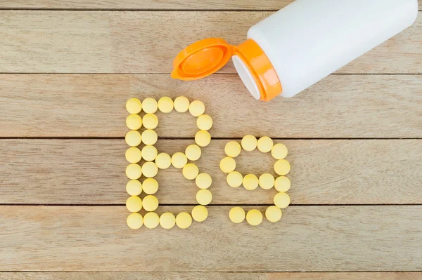 Yellow pills forming shape to B9 alphabet on wood background — Stock Photo, Image