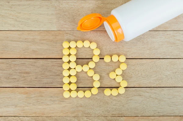 Pílulas amarelas formando forma para B3 alfabeto no fundo de madeira — Fotografia de Stock