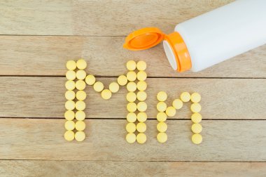 Yellow pills forming shape to Mn alphabet on wood background clipart
