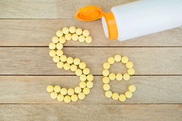 Gelbe Pillen bilden eine Form, um das Alphabet auf Holz-Hintergrund zu schreiben — Stockfoto
