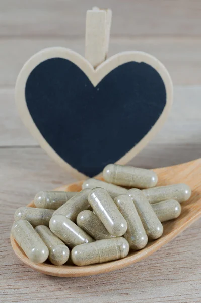 Капсульные таблетки в деревянной ложке с чистой доской в форме сердца — стоковое фото
