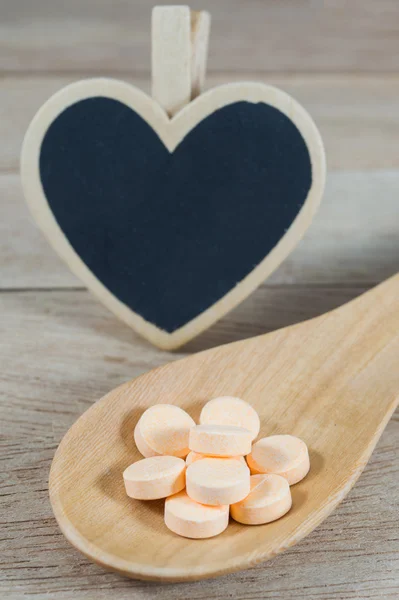 Pastel pílulas laranja em colher de madeira com forma de coração em branco preto — Fotografia de Stock