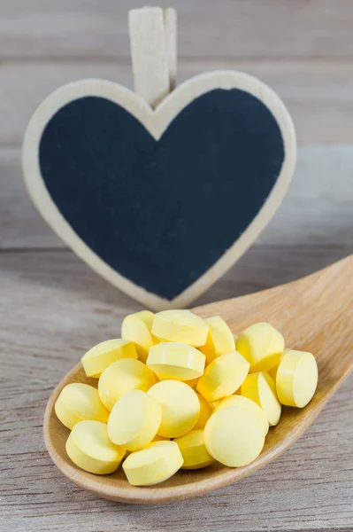 Желтые таблетки в деревянной ложке с чистой доской в форме сердца — стоковое фото