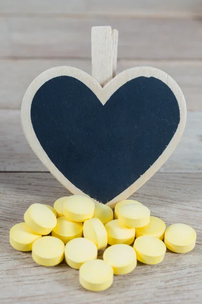 Pílulas amarelas com forma de coração em branco blackboard em backgrou de madeira — Fotografia de Stock