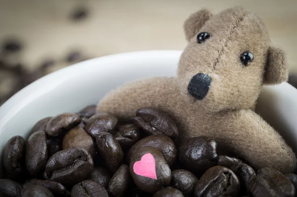 Pequeno urso marrom e grãos de café em caneca branca — Fotografia de Stock