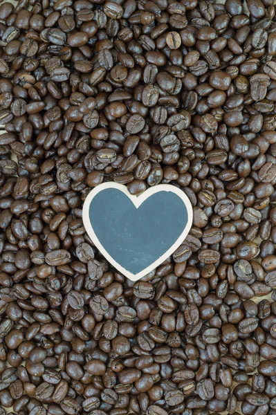 Маленькая доска в форме сердца на фоне кофейных зерен — стоковое фото