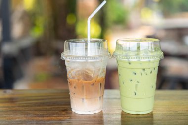 İki ferahlatıcı içecek: pipetli buzlu kahve latte ve buzlu kibrit yeşil çay. Açık bir kafede, sade, ahşap bir masaya yerleştirilmiş..