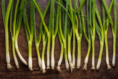 Tahta bir yüzeye dizilmiş yeşil soğanlar.