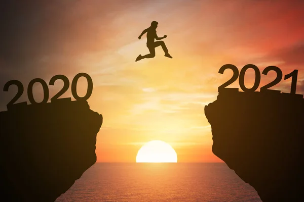 Silüet adam 2020 'den 2021' e gün batımı veya gündoğumu arkaplanıyla dağdan atlıyor. Yeni yıl 2021 konseptiyle mutlu ve başarı artışı