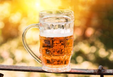 Hafif bira büyük bardakta, alkol arka planda.