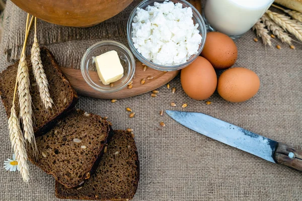 Alimento ecológico leche, pan, huevos, queso, mantequilla, cuchillo, acostado sobre la mesa, sobre el fondo de un campo de trigo. — Foto de Stock
