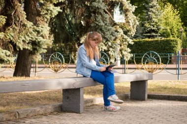 Bankta oturan ve tablet kullanarak uzun saçlı Genç kız 