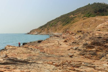 Sahilde kayalar var. Arka planda mavi su, ada ve gökyüzü var. Doğa yolculuğu konsepti