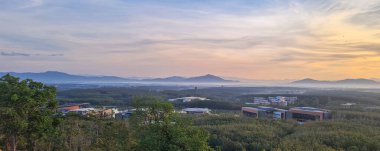 Dağların ve ağaçların üzerinde sabah bulanıklığı. Gökyüzündeki ilk ve son gün ışığı, arka plan olarak güzel kırmızı ve sarı bulutlar. Etrafında beyaz sis var. Dağdaki konsept köy. ve dağın en üst manzarası.
