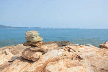 Yukarıdan görülen kayaların üzerinde, arka plan olarak mavi deniz, ada ve gökyüzü bulunur. Çevre turizmi kavramı.