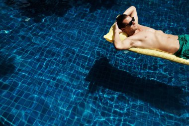 Mavi bir havuzda, lilonun üzerinde yüzen rahat genç bir adamın fotoğrafı.