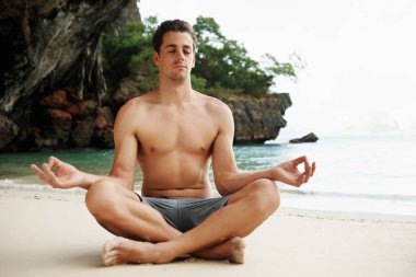 Plajda lotus pozisyonu üzerinde çalışan genç bir adamın kesikli çekimi.