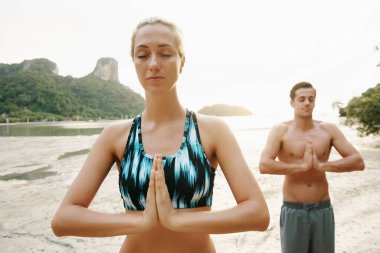 Sahilde yoga yapan genç bir çiftin görüntüsü.