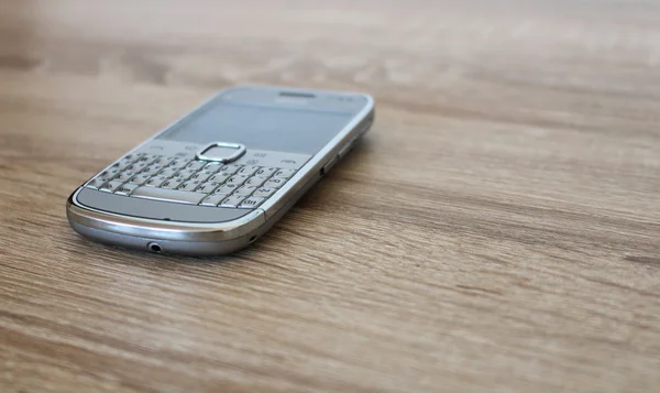 Srebrny telefon komórkowy na drewnianym stole — Zdjęcie stockowe