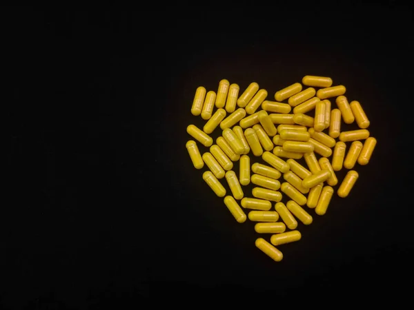 Μια Χούφτα Κίτρινες Κάψουλες Σχήμα Καρδιάς Μαύρο Φόντο Αντιγράψτε Χώρο — Φωτογραφία Αρχείου