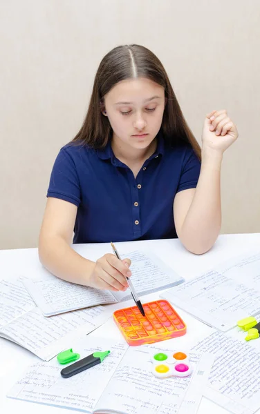 Concentrated teenage girl is playing with popit anti stress toy while studying for exams. — Stock Photo, Image