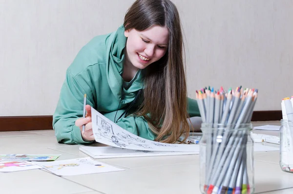 Μια λευκή έφηβη είναι ξαπλωμένη στο πάτωμα και ζωγραφίζει με μολύβια, γελώντας. Αντιγραφή φόντου χώρου. — Φωτογραφία Αρχείου
