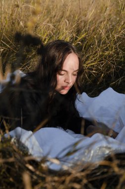 Siyah elbiseli genç esmer kadın altın saat boyunca kuru çimlerin üzerinde beyaz bir battaniye üzerinde yatıyor..