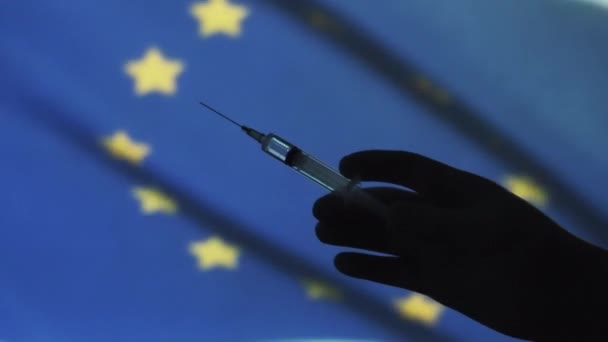 对结肠病毒的疫苗接种 在欧洲联盟旗帜的背景下 用注射器和注射疫苗的男人的手的轮廓 欧盟的疫苗接种 — 图库视频影像
