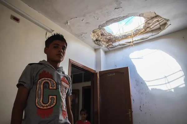 The boy shows a damaged house in which he had to live because of the war — Stock Photo, Image