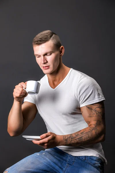 Κομψό αθλητικό άνδρα χαμογελώντας, κρατώντας φλιτζάνι καφέ. Συνεδρίαση. — Φωτογραφία Αρχείου