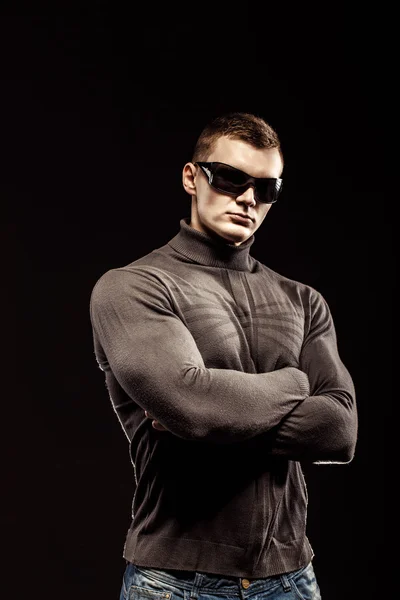 Combattimento muscoloso azione eroe uomo indossa maglione marrone e occhiali da sole. Studio girato . — Foto Stock