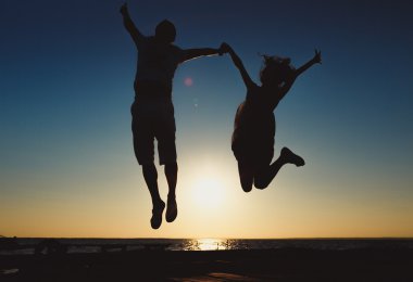 Uzun zamandır beklenen tatil konsepti: günbatımı deniz sahilde bir atlamada genç çift.